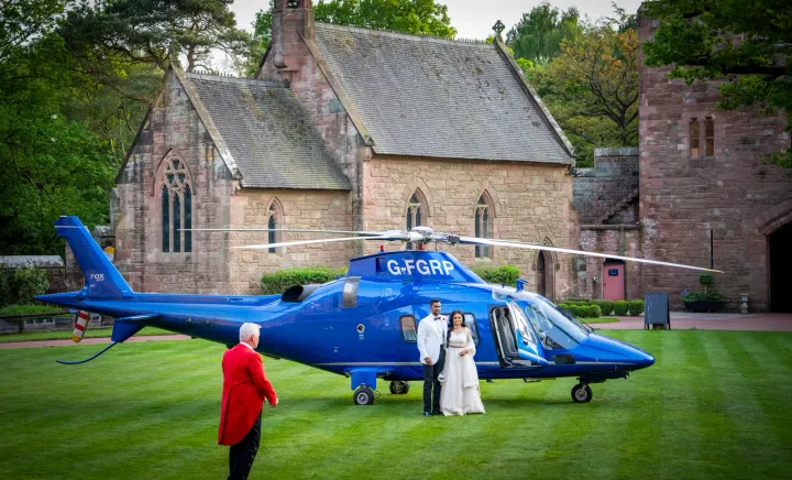 Wedding guests beside a helicopter at a stone venue