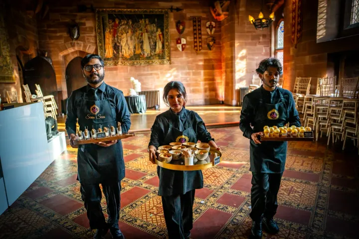 Three servers presenting canapés in a historic hall