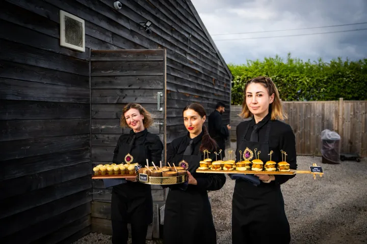 Servers carrying canapés outside a timber-clad venue