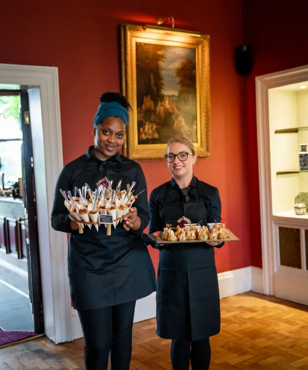 Two servers with canapé trays in an ornate room