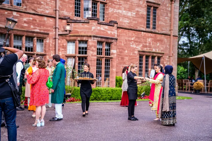 Servers welcoming guests outside a brick manor house
