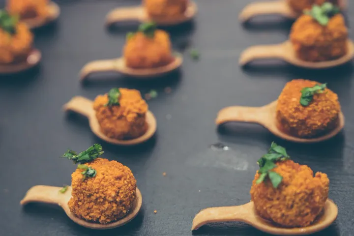 Golden savoury bites with herb garnish on tasting spoons