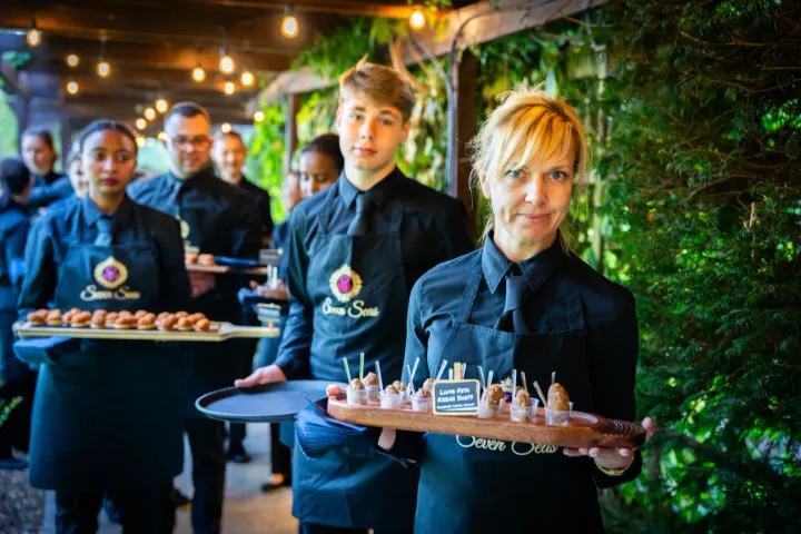 Catering team with canapé trays beneath festoon lights