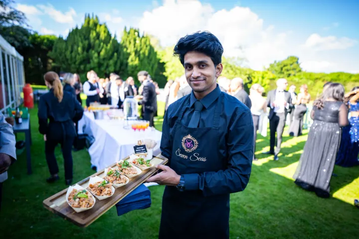 Server offering canapés on a garden lawn
