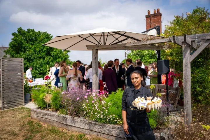Server carrying savoury cones through a garden reception